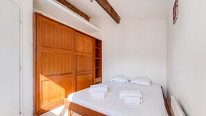 A bedroom with a wooden wardrobe, a bed with white linens, and a radiator. - Le Pescadou - Terrasse vue mer (Marseille)