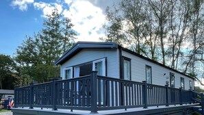 A mobile home with a fenced deck, a paved driveway, and a grassy area. - Luxurious and Cosy Holiday Lodge in the New Forest National Park (Landford)