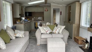 A cozy living room with a sofa and ottoman, a kitchen with wooden cabinets, and a dining area with a table and chairs. - Luxurious and Cosy Holiday Lodge in the New Forest National Park (Landford)