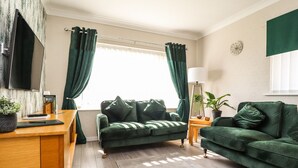 Una sala de estar moderna con un sofá verde, una mesita de madera, una lámpara de pie y un televisor montado en la pared.