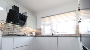 Una cocina moderna con armarios blancos, una campana extractora negra y un ventanal con persianas.