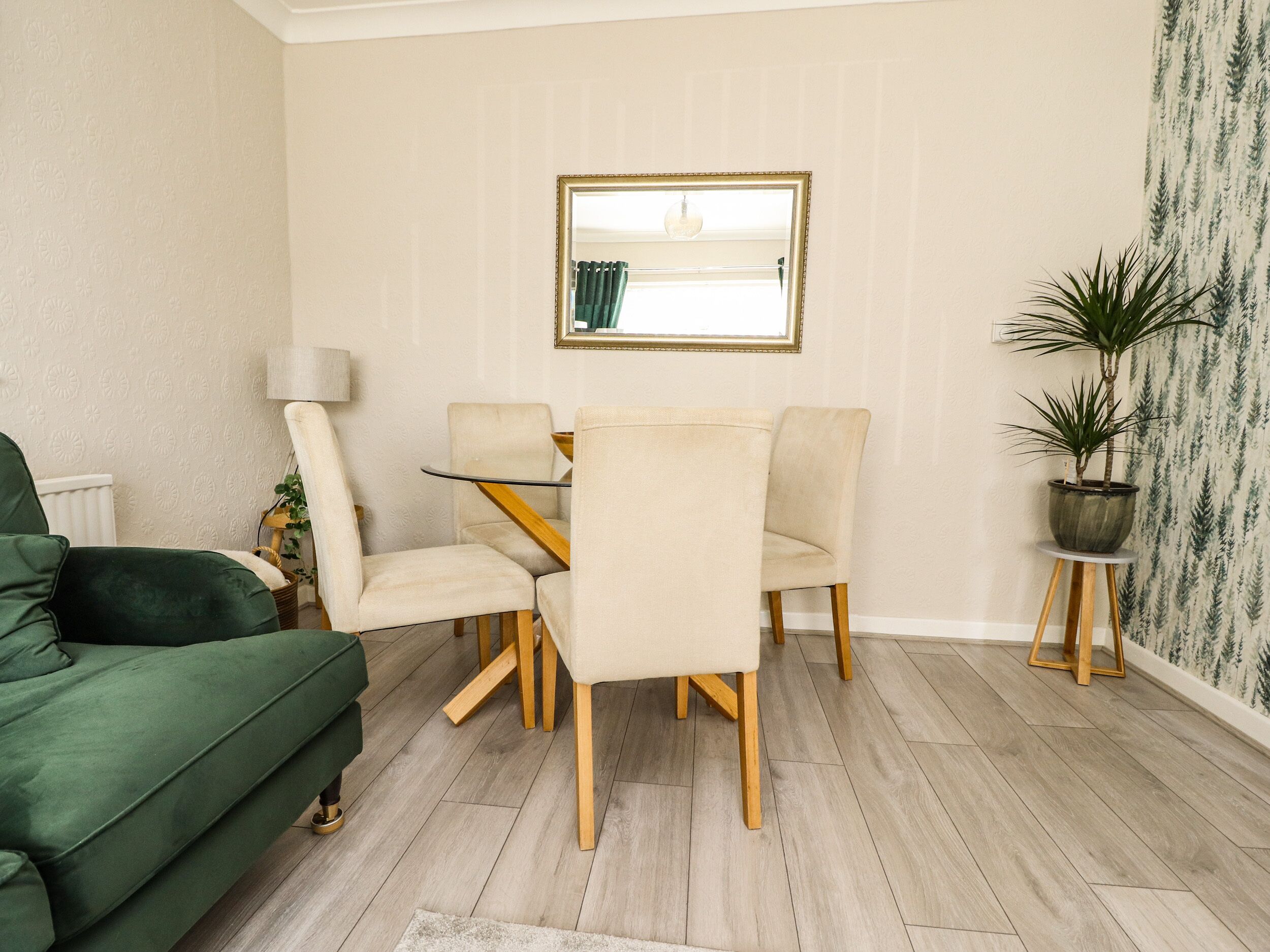 Un coin repas avec une table et des chaises, un canapé vert, une lampe et une plante en pot.
