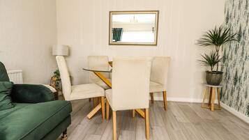 Uma sala de jantar com uma mesa, cadeiras, um sofá verde, um abajur e um vaso de planta.