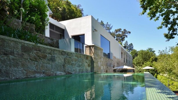 A modern house with a swimming pool, stone wall, and greenery.