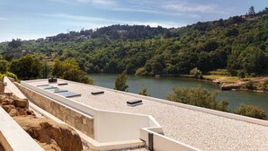 A rooftop terrace with a view of a river and forested hills.