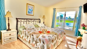 Un dormitorio con cama, mesitas de noche, ventana con cortinas, un cuadro en la pared y televisión en la pared.