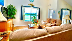 Una sala de estar con un sofá, una mesa de centro, un televisor, un reloj y una ventana con cortinas.