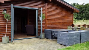 Une cabane en bois dotée d’une porte coulissante en verre qui donne sur un intérieur comprenant un canapé et une table à manger.