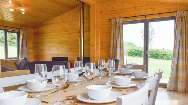 Une table à manger dressée pour un repas dans un chalet en bois, avec vue sur le paysage extérieur.