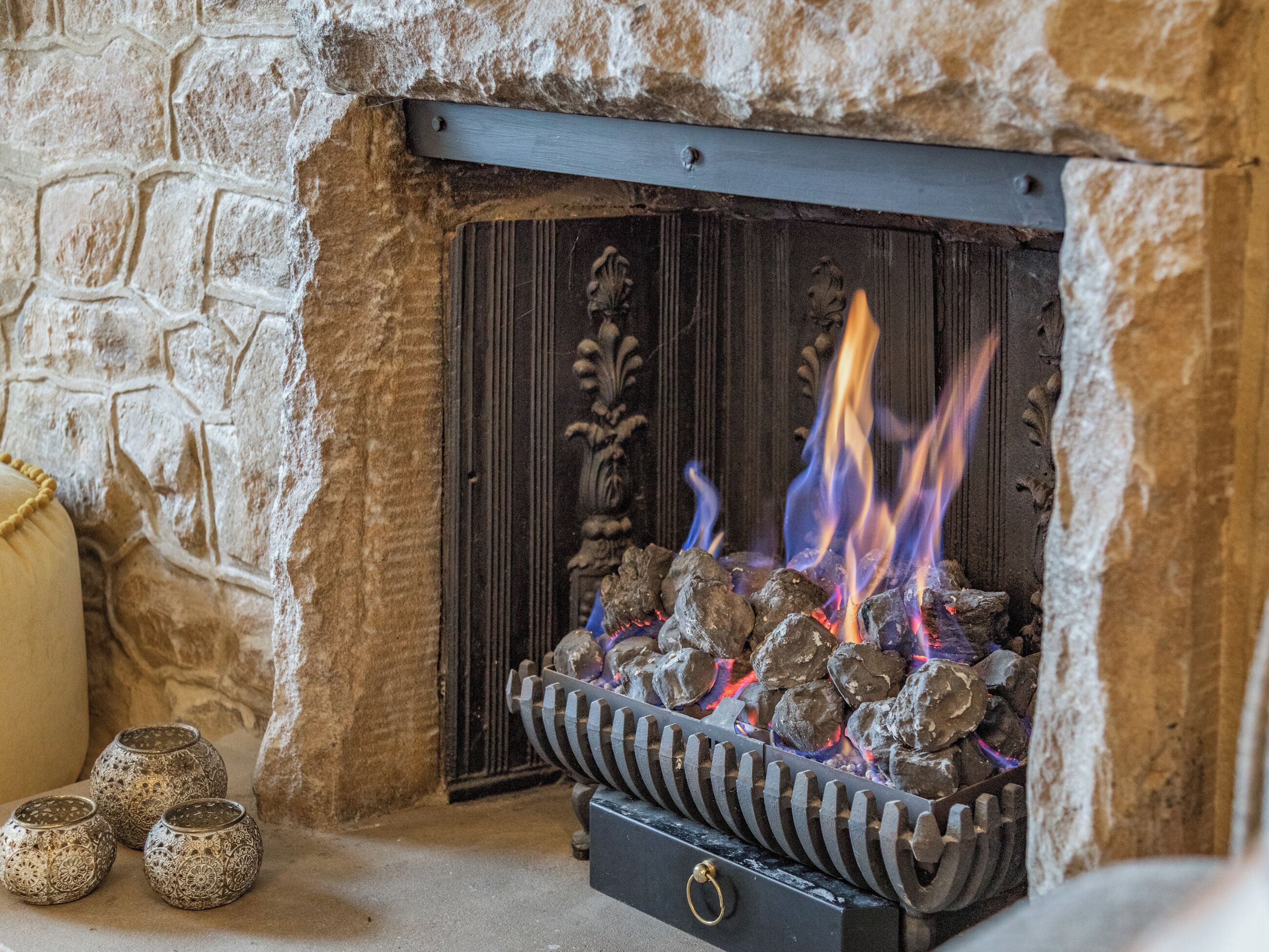 A stone fireplace with a metal grate, burning logs, and decorative metal spheres.