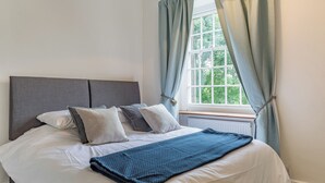 Ein Schlafzimmer mit Bett, einem Fenster mit Vorhängen, einem Heizkörper und Blick ins Grüne.