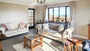 A living room with two sofas, a coffee table, and a side table. There is a window with curtains and a view of the outdoors. - 4 bedroom accommodation in Winscales (Winscales)