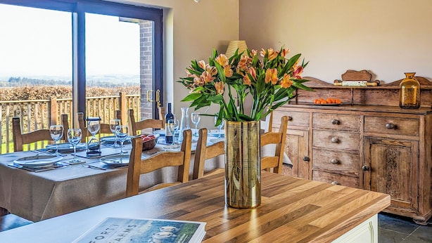 A dining area with a wooden table set for four, a vase with flowers, and a book titled "Forty Farms Amy Bateman" on the table. - 4 bedroom accommodation in Winscales (Winscales)