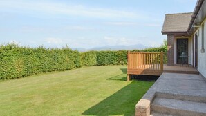 A residential property with a well-maintained lawn, a wooden deck, and a brick exterior. - 4 bedroom accommodation in Winscales (Winscales)