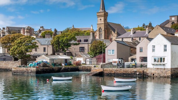 Une ville côtière dotée d’un clocher d’église imposant, d’eaux calmes et de petits bateaux.
