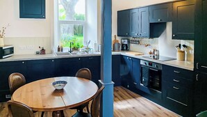 Une cuisine moderne avec des meubles de couleur sombre, une table à manger en bois et des luminaires suspendus.