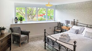 Une chambre à coucher comprenant un lit, une chaise, un bureau, une lampe et une fenêtre donnant sur des arbres et des immeubles.