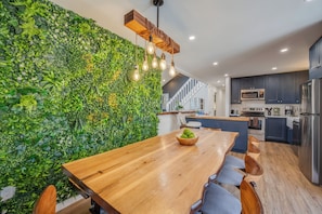 A modern kitchen with a wooden dining table, a green vertical garden wall, and stainless steel appliances.