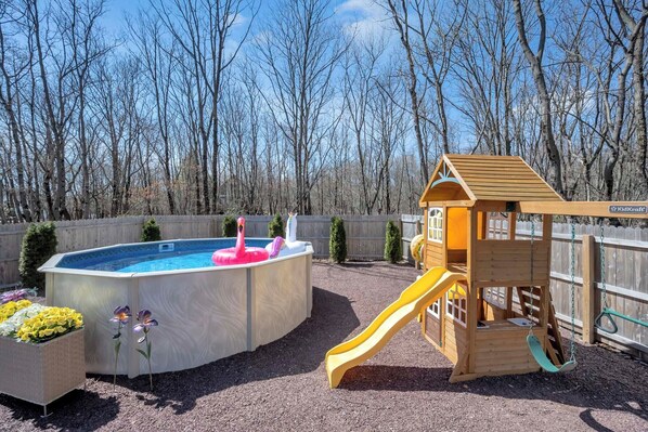 Un jardin avec une cabane en bois, un toboggan et une piscine hors sol agrémentée de jeux gonflables.