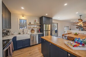Une cuisine moderne avec des meubles de couleur sombre, des appareils en acier inoxydable et un îlot central en bois où l’on peut prendre des collations.