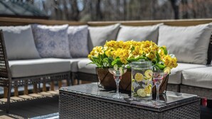 A wicker table with a glass pitcher and two martini glasses, a potted plant with yellow flowers, and a wicker sofa with cushions. - Private Pool- Hot Tub- Playground- Fire Pit- Fenced In Backyard- Pets! (Pocono Mountains)