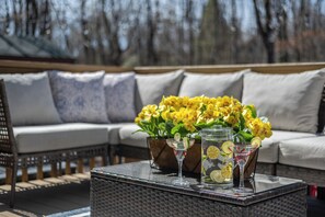 A wicker table with a glass pitcher and two martini glasses, a potted plant with yellow flowers, and a wicker sofa with cushions.
