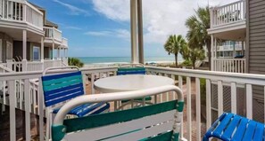 A balcony with a table and chairs, overlooking a beach with palm trees and a clear sky. - Admiral Quarters II #14 (Surfside Beach)