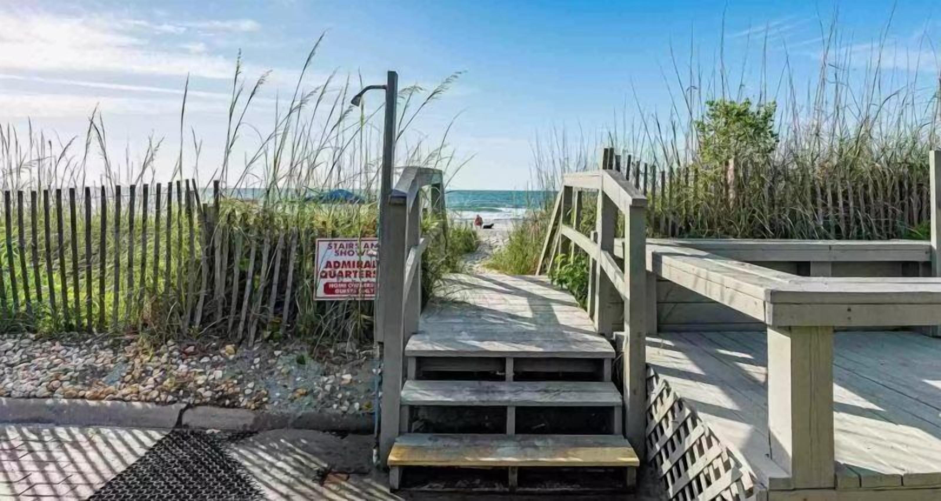 Een houten trap die leidt naar een strandgedeelte, met een bord waarop staat 'STAIRS AM SHOW ADMIRAL QUARTER'.