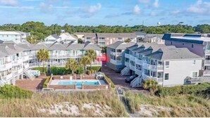 A coastal residential area with multi-story houses, a swimming pool, and a beach in the background.