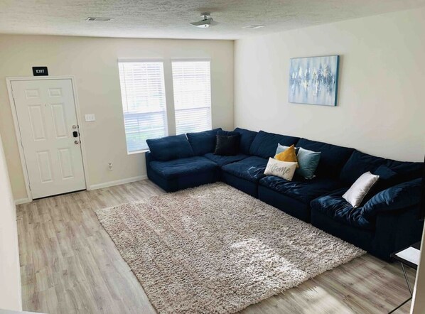 A living room with a dark blue sectional sofa, a light-colored shag rug, and a painting on the wall.