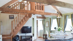 A spacious living area with a wooden staircase, a flat-screen TV, and a dining area with a table and chairs.