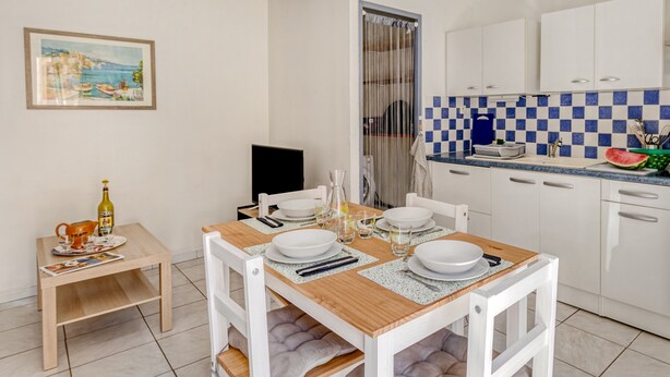 A small, clean kitchen with white cabinets, a checkered backsplash, and a dining table set for four.