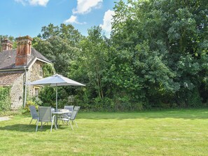 A stone house with a brick chimney, a lawn, and a table with chairs under a large umbrella.