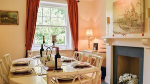 Comedor con una mesa redonda para cuatro personas, chimenea y ventana con cortinas.
