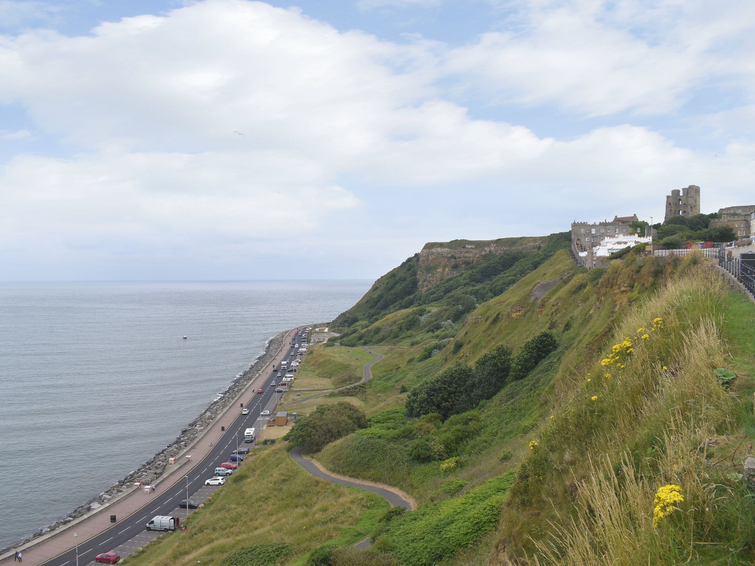 A coastal road with a castle on a hill, a beach, and a clear sky.