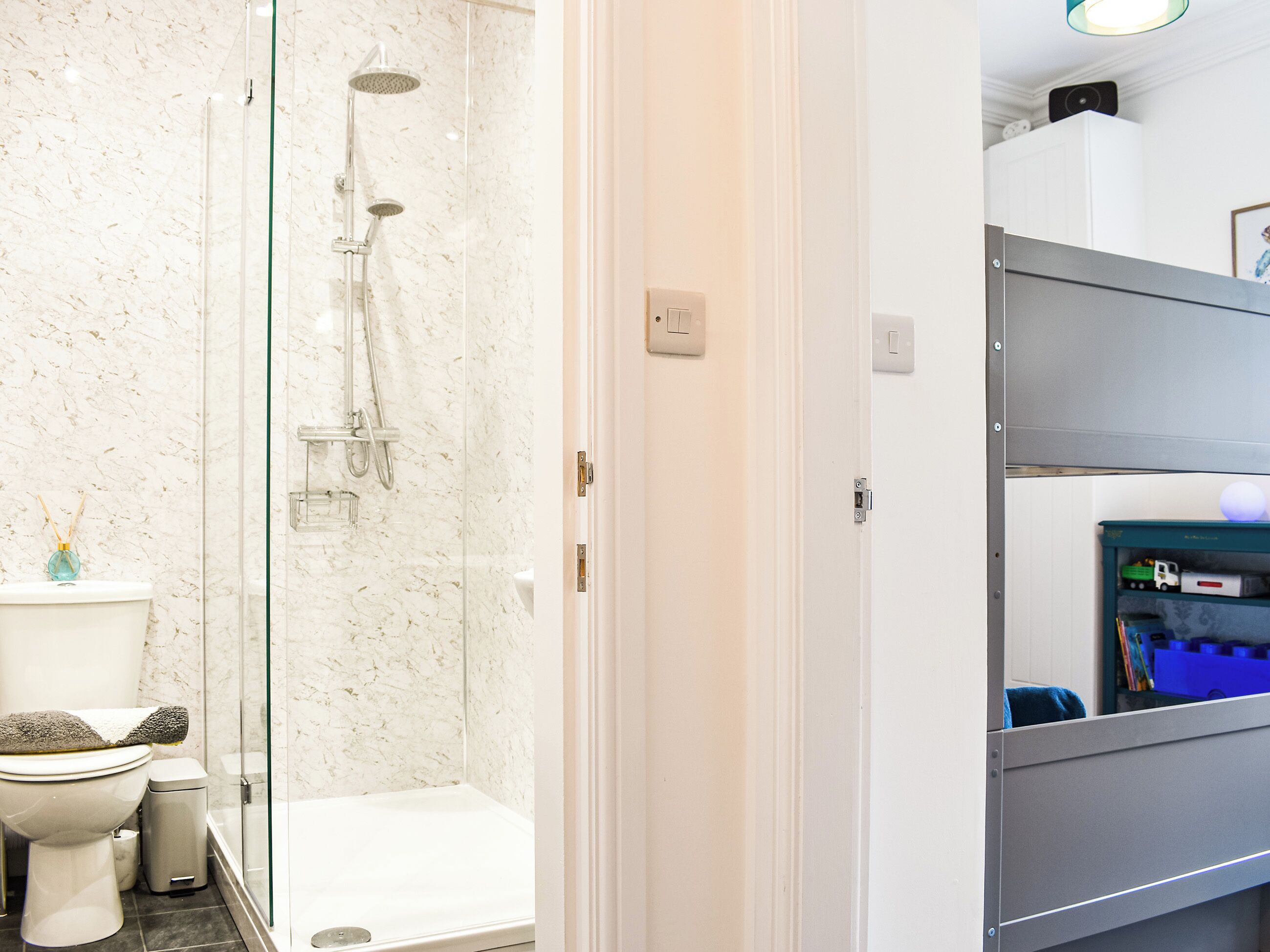 A bathroom with a glass-enclosed shower, a toilet, and a storage unit with toys.
