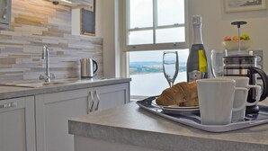 Una cucina moderna con vista sul mare, una moka, un croissant e una bottiglia di vino.