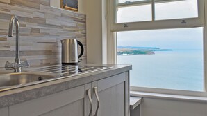 Una cucina con un bollitore in acciaio inossidabile sul bancone, un rubinetto moderno e vista mare attraverso una finestra.