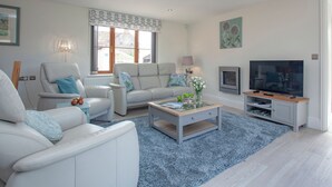 A modern living room with a sofa, armchairs, a coffee table, a TV, and a fireplace.