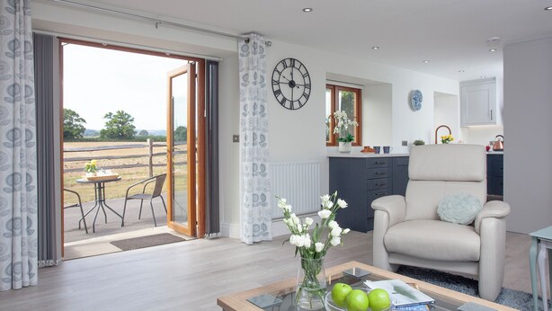 A modern living room with a glass coffee table, a sofa, and a dining area with a view of the countryside.