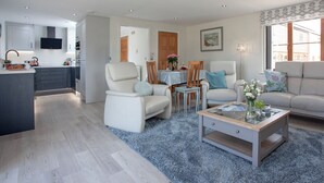 A modern living room with a sofa, armchairs, a coffee table, and a kitchen area with cabinets and a television.