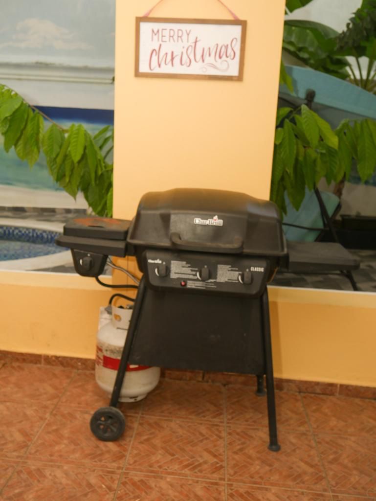 Een draagbare grill met gasfles en wielen, op een betegelde vloer geplaatst.