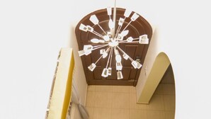 Eine Wendeltreppe mit einer zentralen Leuchte, einer gelben Wand und einer kleinen Pflanze auf der Zwischenebene.