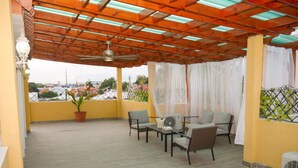 Eine überdachte Terrasse im Freien mit Deckenventilator, Tisch mit Stühlen und einer Topfpflanze.