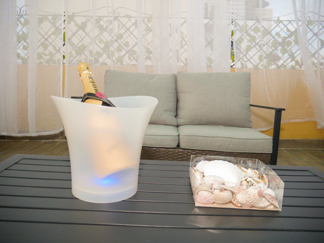 A room with a glass table, a bottle of champagne, and a plastic bag of seashells.