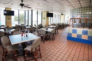 Un amplio comedor interior con varias mesas y sillas, ventanas grandes y ventiladores de techo.
