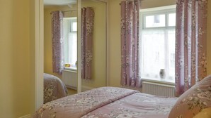 Une chambre à coucher avec une literie à motifs floraux, un radiateur et une fenêtre avec des rideaux.