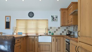 A kitchen with wooden cabinets, a sink, and a stove. There is a clock on the wall and a picture of a cow. - 2 bedroom accommodation in Catsham, near Glastonbury (Catsham, near Glastonbury)