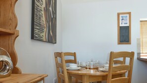 A dining area with a wooden table set for four, surrounded by wooden chairs. There is a wooden cabinet with drawers to the left. - 2 bedroom accommodation in Catsham, near Glastonbury (Catsham, near Glastonbury)