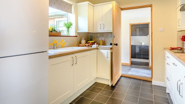 Una cocina moderna con armarios blancos, piso de baldosas negras y una puerta de madera que da a otra habitación.